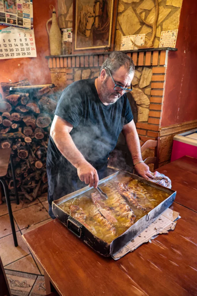 A local chef preparing a hearty, traditional meat dish in a rustic Andalusian restaurant, highlighting the authentic gastronomy on our motorcycle tours | Un chef local preparando un abundante plato de carne tradicional en un restaurante rústico andaluz, destacando la auténtica gastronomía de nuestras rutas en moto.