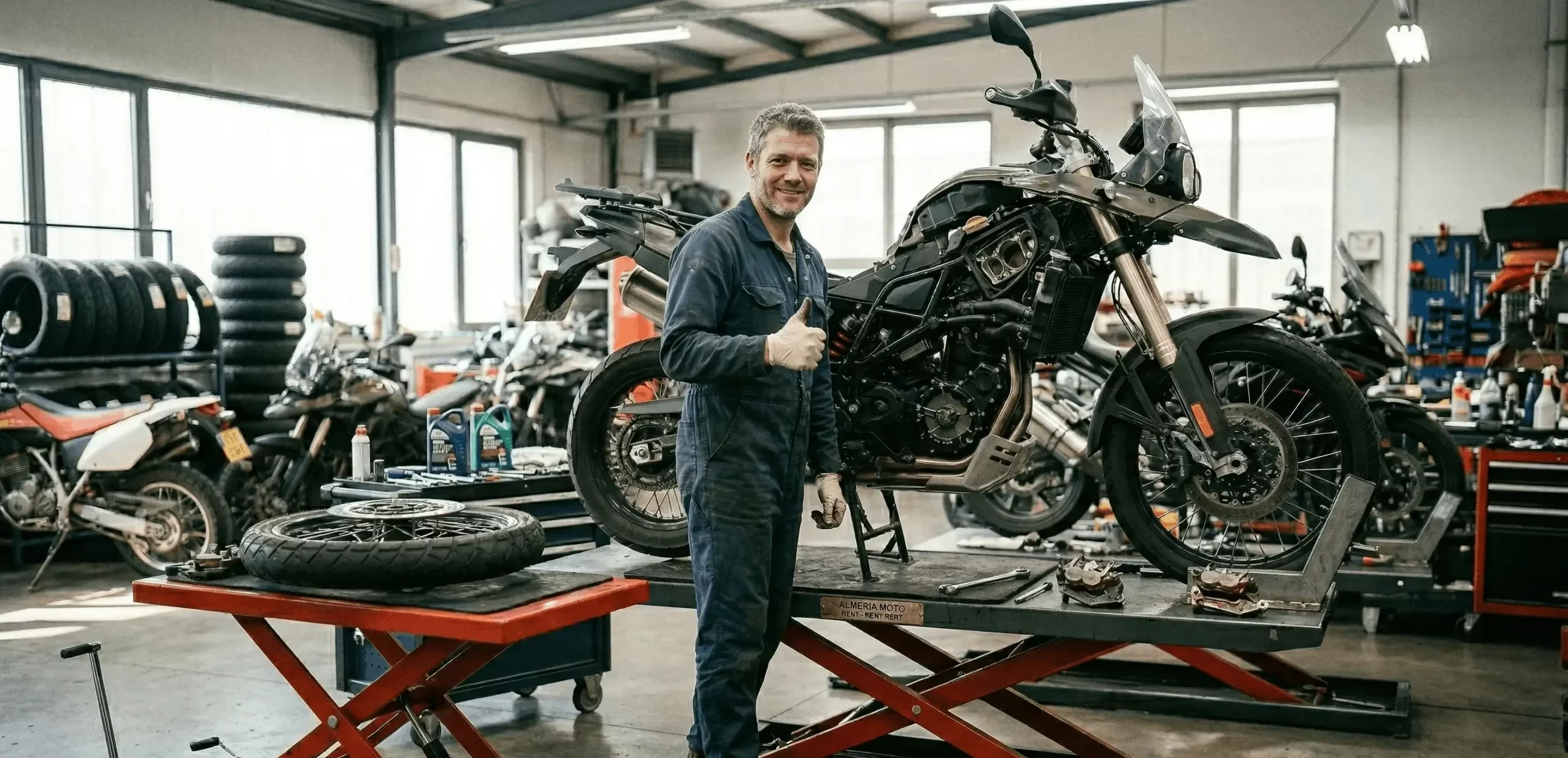 Professional in-house motorcycle mechanic giving a thumbs up next to a serviced adventure bike in our Almeria rental workshop | Mecánico profesional dando un pulgar hacia arriba junto a una moto trail en nuestro taller de alquiler en Almería