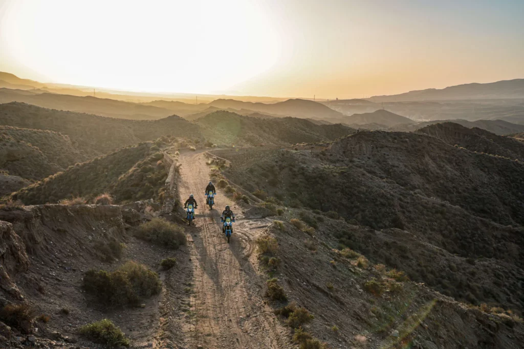 Three adventure motorcyclists riding along a rugged dirt ridge at sunset in the Tabernas Desert, Almeria | Tres pilotos de moto trail recorriendo una escarpada cresta de tierra al atardecer en el Desierto de Tabernas, Almería