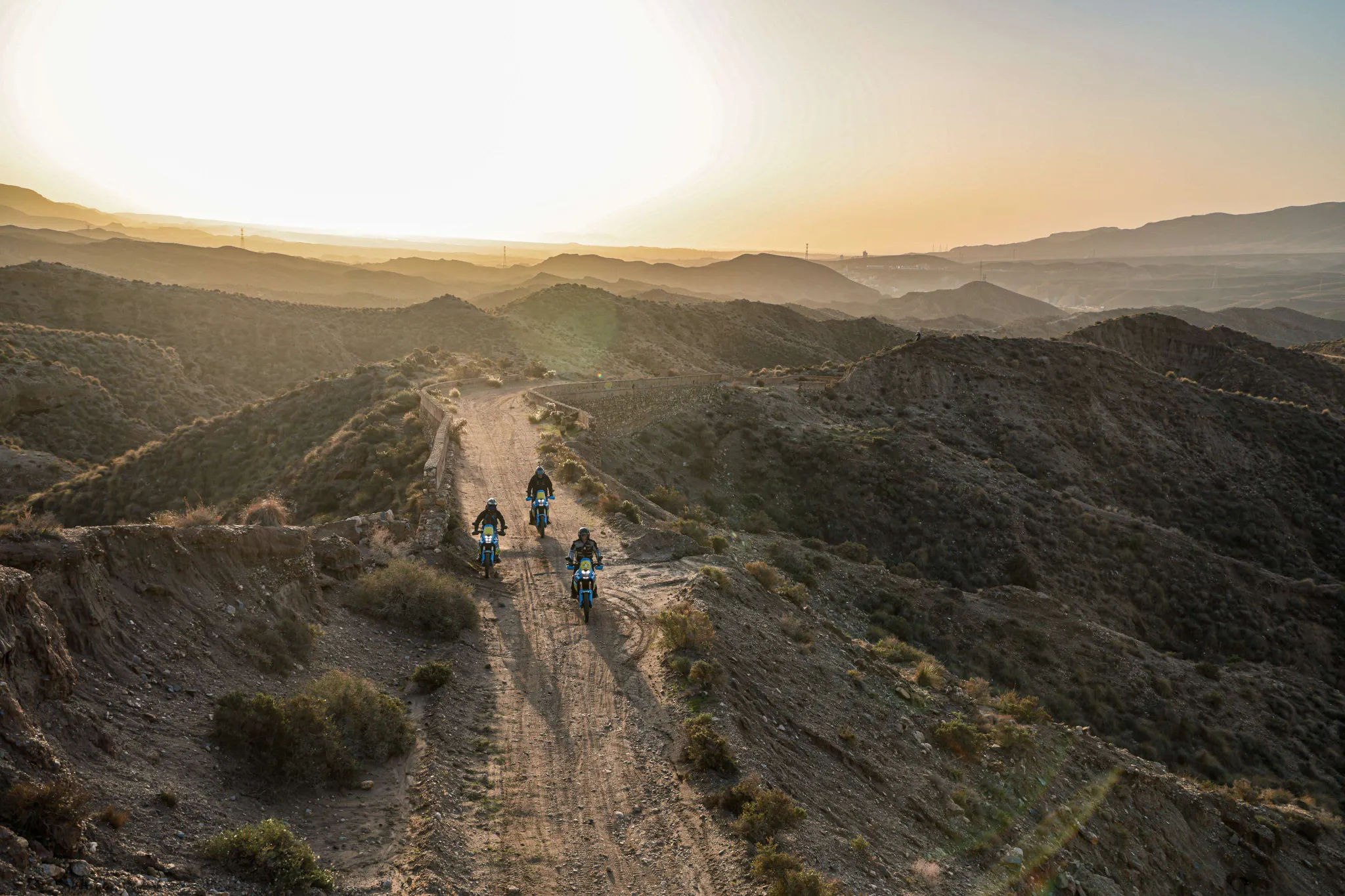 Three adventure motorcyclists riding along a rugged dirt ridge at sunset in the Tabernas Desert, Almeria | Tres pilotos de moto trail recorriendo una escarpada cresta de tierra al atardecer en el Desierto de Tabernas, Almería