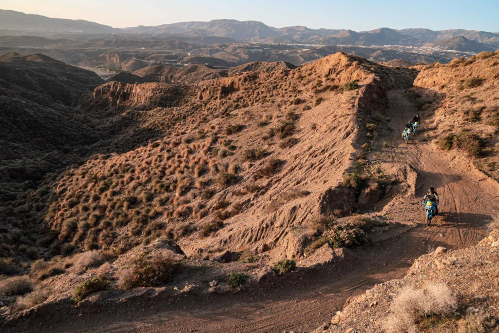 Three adventure motorcyclists riding down a rugged dirt trail in the spectacular mountain landscape of the Tabernas Desert in Almeria | Tres pilotos de moto trail recorriendo una ruta de tierra en el espectacular paisaje montañoso del Desierto de Tabernas en Almería