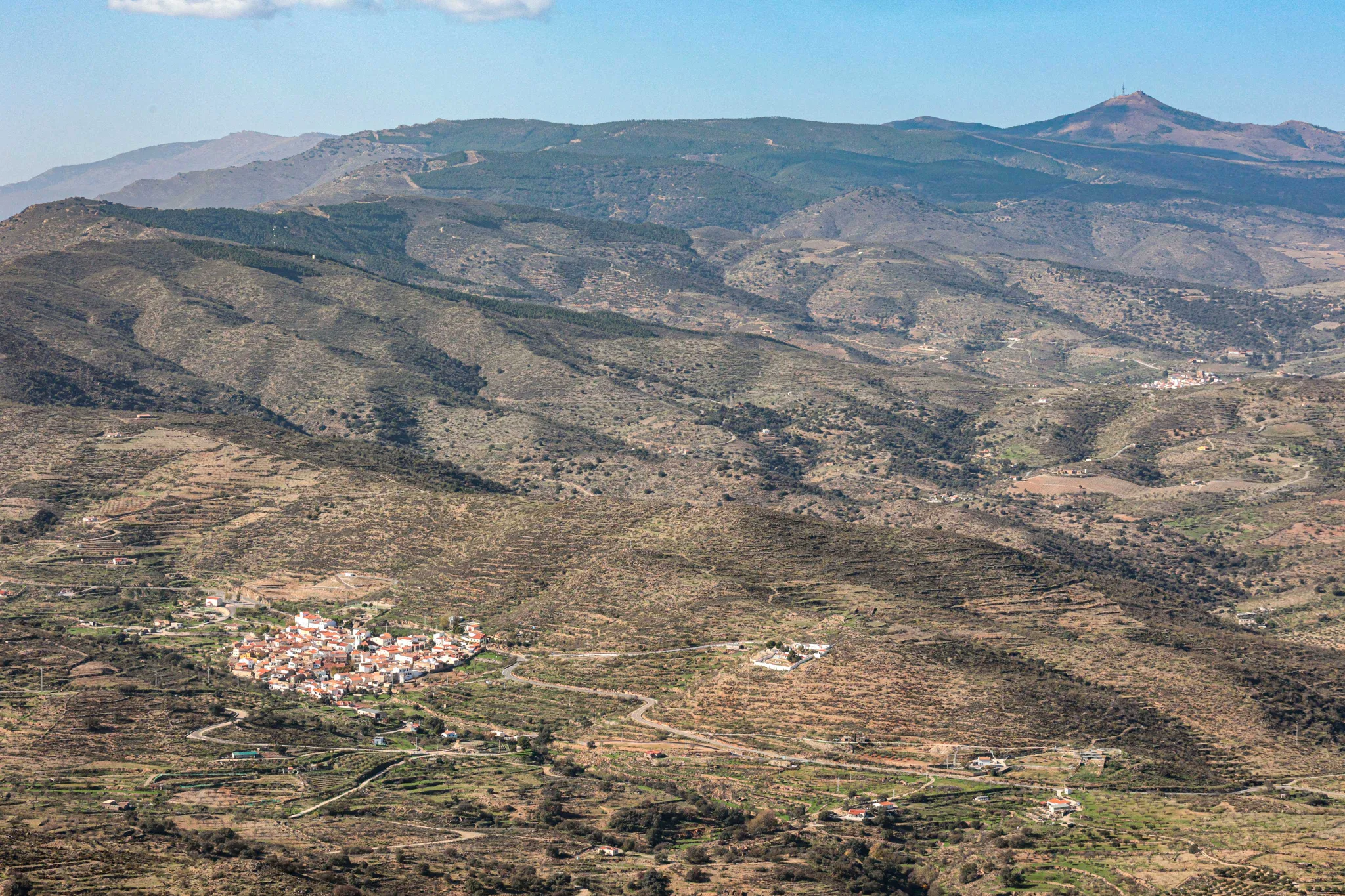 A sprawling view of rugged mountains and a traditional white village nestled in a valley in Andalusia, Spain, showcasing the vast, remote landscapes explored on our adventure motorcycle tours. | Una vista panorámica de montañas escarpadas y un tradicional pueblo blanco en un valle de Andalucía, España, mostrando los vastos y remotos paisajes que exploramos en nuestras rutas en moto trail.