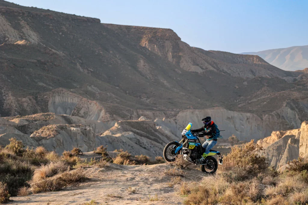 An adventure motorcycle rider climbing a rugged dirt ridge in the Tabernas Desert of Andalusia, Spain, during an extreme off-road motorcycle tour. | Un piloto de moto trail subiendo una cresta de tierra escarpada en el Desierto de Tabernas en Andalucía, España, durante una ruta extrema en moto off-road