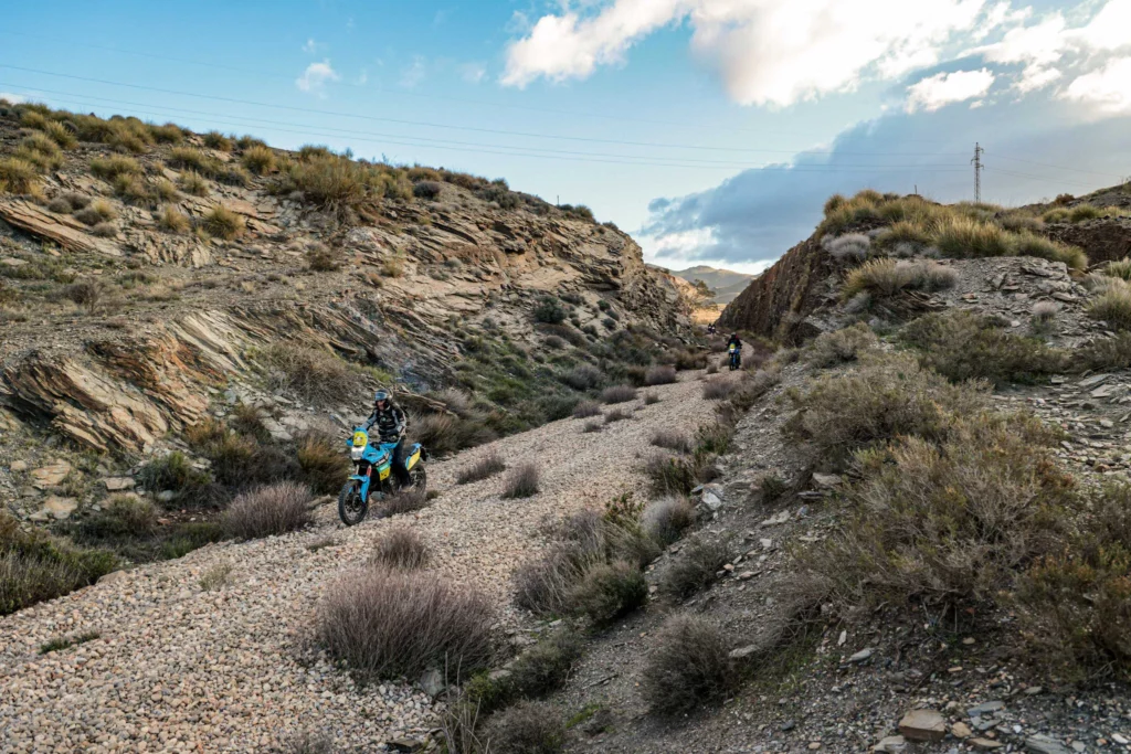 Group of adventure motorcycle riders navigating a rocky dry riverbed canyon during a guided off-road tour in Andalusia, Spain.